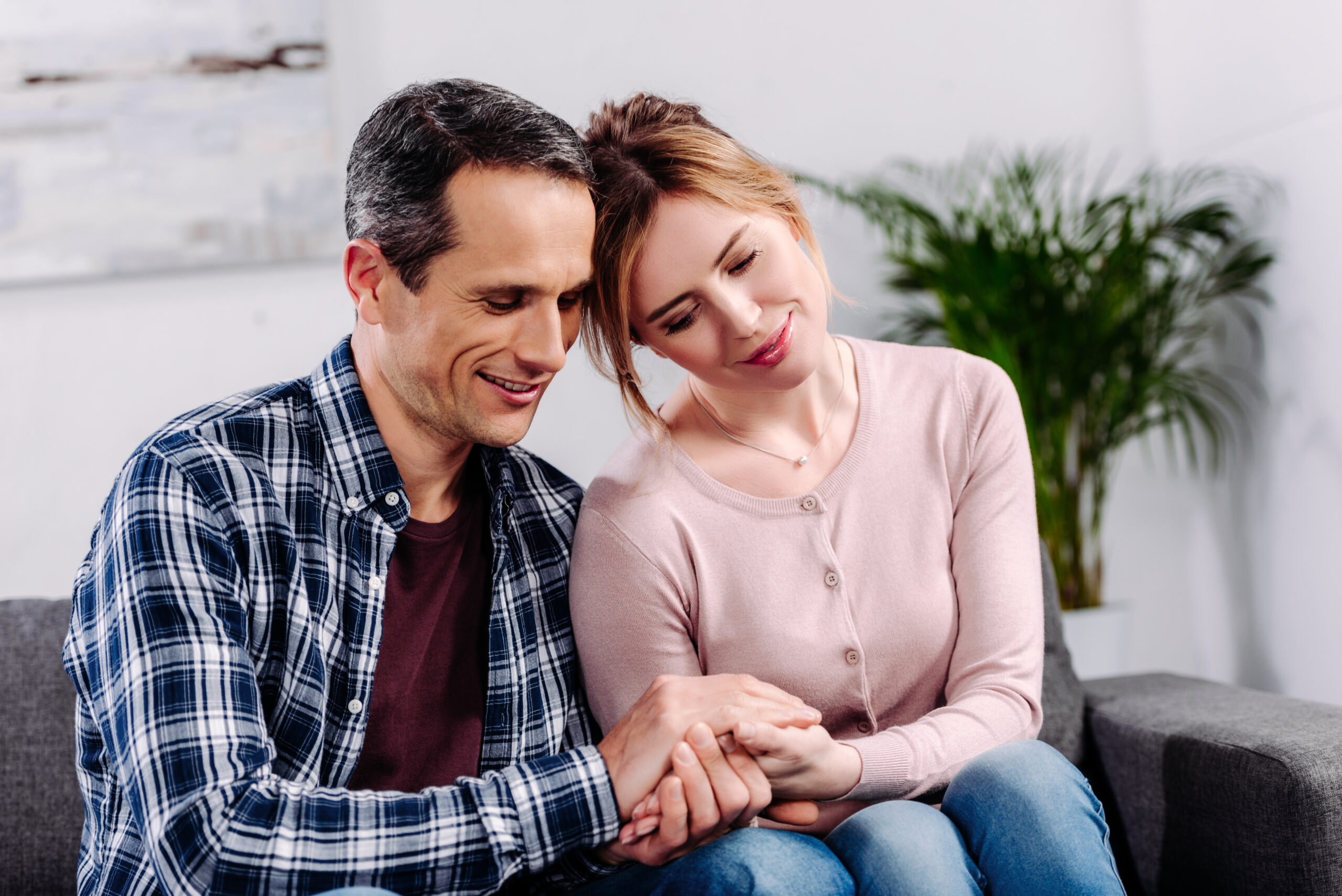 wife and husband holding hands while resting on sofa at home